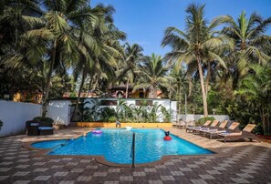A swimming pool surrounded by palm trees and lounge chairs. - Amor Beach Resort (Candolim)