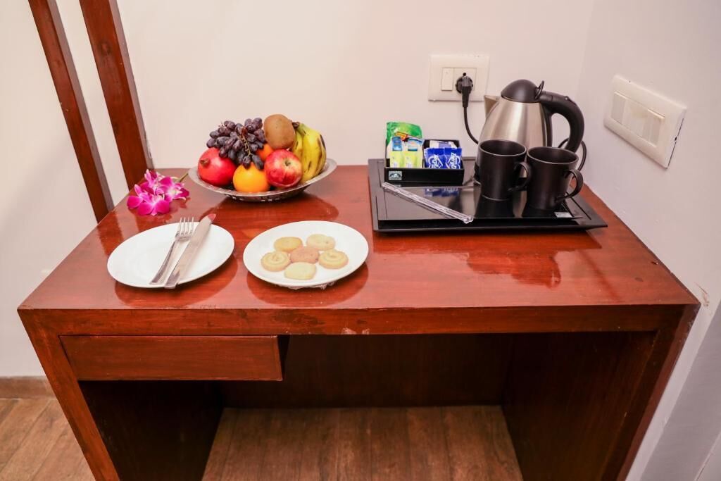 Un bureau en bois sur lequel on trouve une assiette de biscuits, une assiette de fruits, une bouilloire et deux tasses.