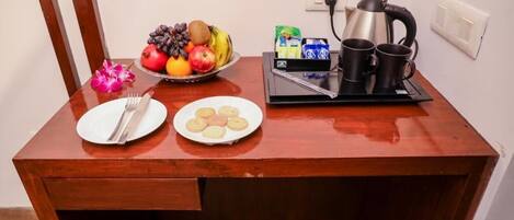 A wooden desk with a plate of cookies, a plate of fruit, a kettle, and two mugs.