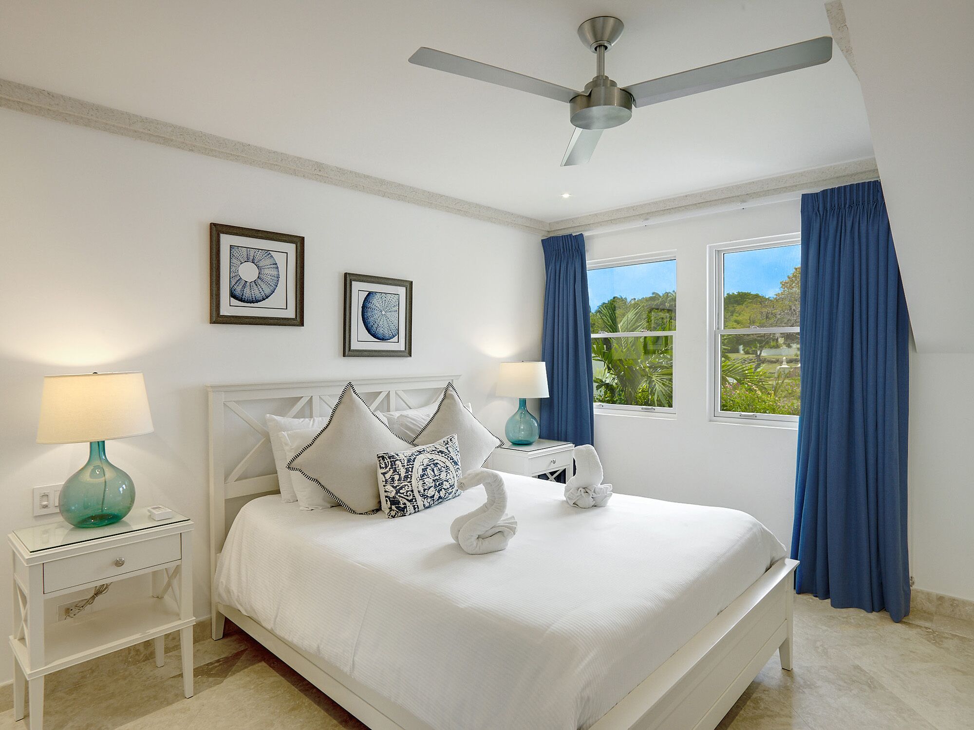A bedroom with a bed, two bedside tables, a ceiling fan, and a window with curtains.