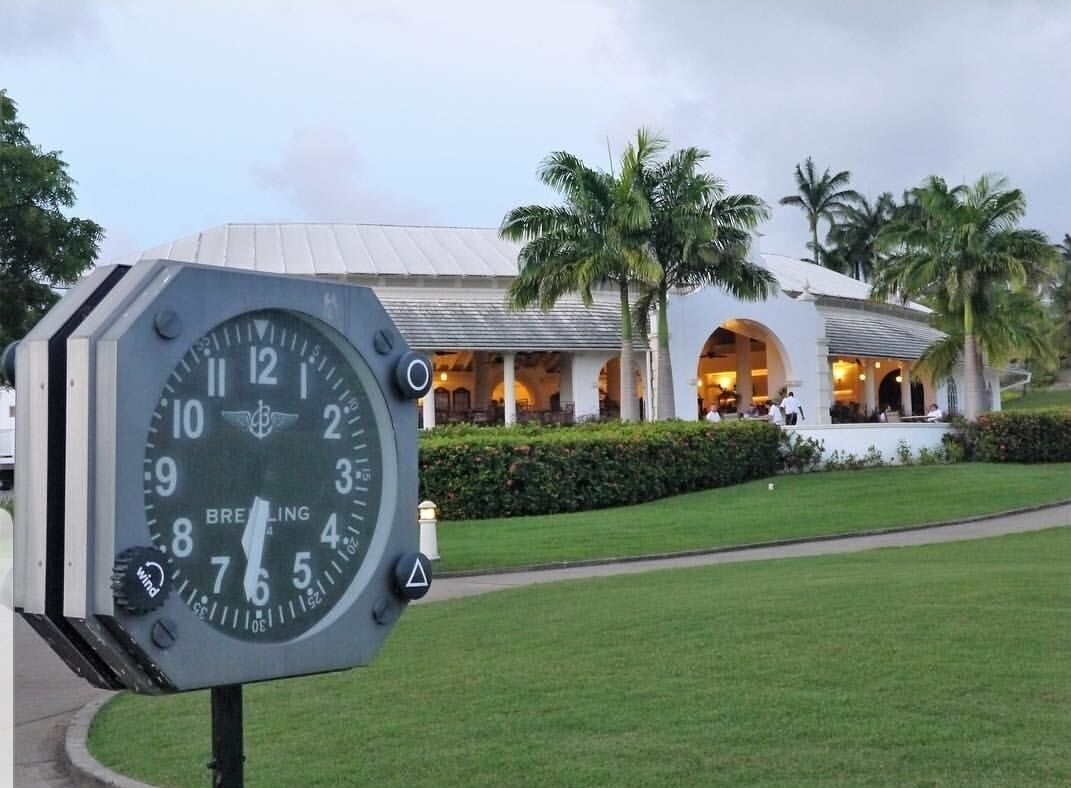 Eine Uhr der Marke „BREITLING“ und im Hintergrund ein Gebäude mit heller Fassade und Rundbogenfenstern.