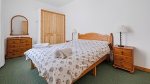 Ein Schlafzimmer mit einem Holzbett, einem Nachttisch, einer Kommode, einem Kleiderschrank und einem Spiegel.