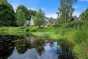 A house with a pond in front, surrounded by greenery and trees. - Aigas Holiday Cottages Old Dairy (By Beauly,, Inverness-shire)
