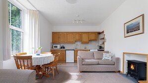 Ein gemütliches Wohnzimmer mit Kamin, ein Essbereich mit Tisch und Stühlen sowie eine Küche mit Holzschränken und Geräten.
