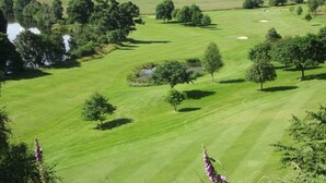 Ein Golfplatz mit Teich, Bäumen und sanften Hügeln im Hintergrund.