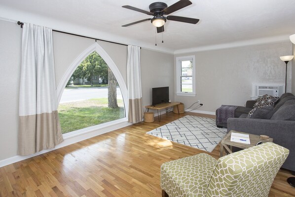 A living room with a large window, a ceiling fan, a sofa, a patterned armchair, a small table, and a TV. - Triangular Casa in Billings (Billings)