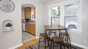 A kitchen with wooden cabinets, a dining table with four stools, a clock on the wall, and a window with a view of a vehicle outside. - Triangular Casa in Billings (Billings)