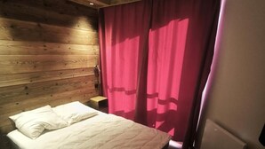 Ein Schlafzimmer mit einem Holzkopfende, einem Bett mit weißer Bettwäsche, einem Nachttisch und einem Fenster mit rosa Vorhängen.