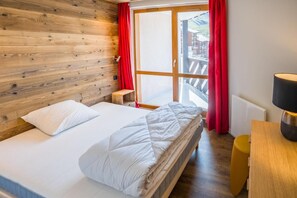 A room with a bed, a small table, a lamp, and a view of the outside.