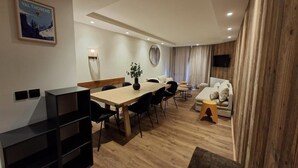 Ein modernes Wohnzimmer mit Holzboden, einer Essecke mit Holztisch und -stühlen, einer Couch und einem an der Wand befestigten Fernseher.