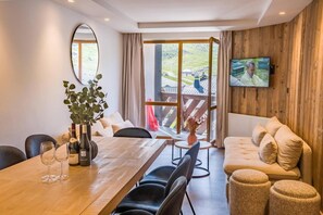 A modern living room with a wooden floor, a dining table with chairs, a sofa, and a television mounted on the wall. - 100m from ski slopes, 3rd floor, sauna, hammam, balcony, tv, 53m², Val Thorens (Val Thorens)
