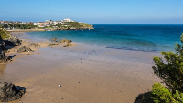 Une plage côtière offrant une vue dégagée sur la mer, avec un bâtiment situé sur une colline en arrière-plan.