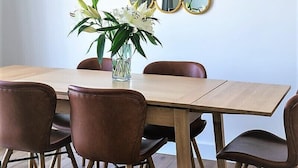 Un coin repas avec une table en bois, six chaises marron et un vase contenant des fleurs blanches.