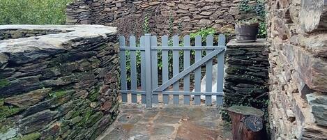 A stone wall with a wooden gate, a stone pathway, and a potted plant.