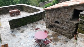 Une terrasse en pierre avec une table ronde et des chaises, un four en pierre et un petit coin salon avec une table et des chaises.