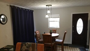 Un salon avec un canapé, une table à manger avec des chaises, une horloge au mur et une porte avec une fenêtre.