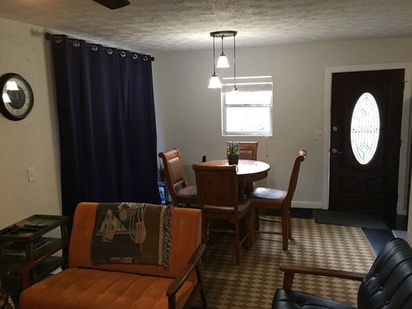A living room with a sofa, a dining table with chairs, a clock on the wall, and a door with a window. - Enjoy the fresh mountain air at 4300 feet! (Maggie Valley)