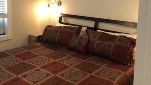 Une chambre à coucher comprenant un lit, un ventilateur de plafond, une lampe fixée au mur et une fenêtre avec des stores.