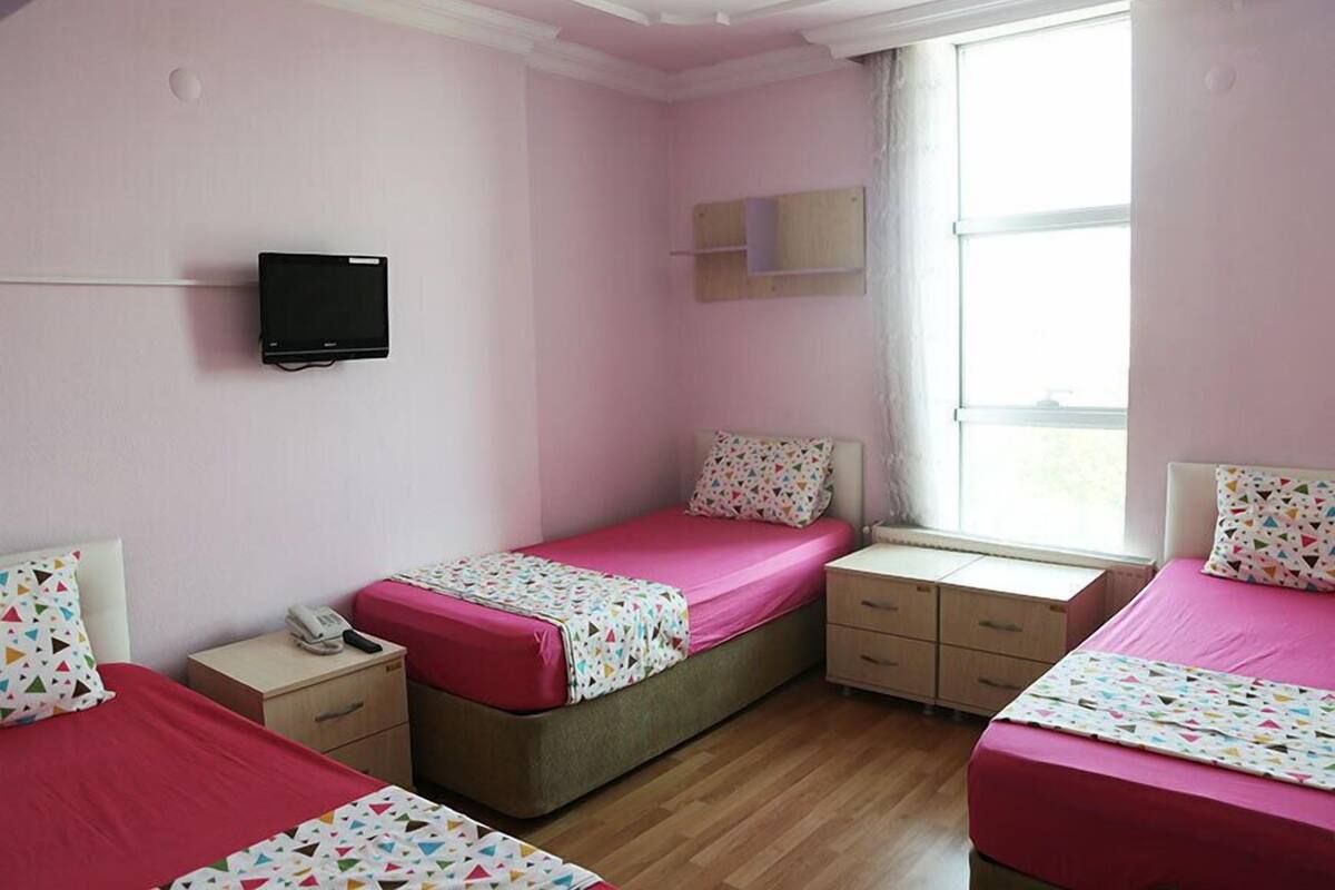 Una habitación con dos camas, un televisor montado en la pared, una ventana y un escritorio pequeño con un teléfono.