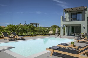 Un espace piscine aménagé sur le toit, avec des chaises longues, une table et un immeuble moderne doté d’un balcon.
