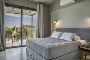 Une chambre moderne avec un grand lit, une table de chevet et une vue sur un balcon aménagé avec du mobilier d’extérieur.