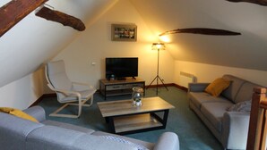 Ein Dachzimmer mit Fernseher, einer Couch, einem Sessel, einem Couchtisch und einer Stehlampe.