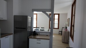 Eine kleine Küche mit Kühlschrank, ein Essbereich mit Tisch und Stühlen sowie eine kleine Arbeitsfläche mit Schreibtisch und Stuhl.