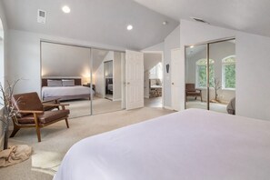 A bedroom with a large bed, a chair, and a wardrobe with a mirror.
