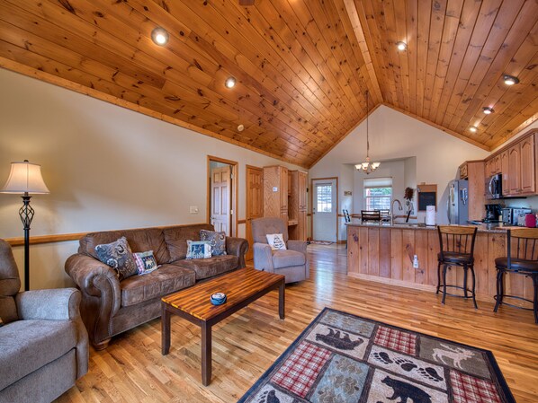 A spacious living area with a wooden ceiling, a sofa, a coffee table, and a kitchen in the background. - 2 BD 2 BA Cottage, Paved Access, Close to Town, Super Views, Cable, WIFI, (Waynesville)