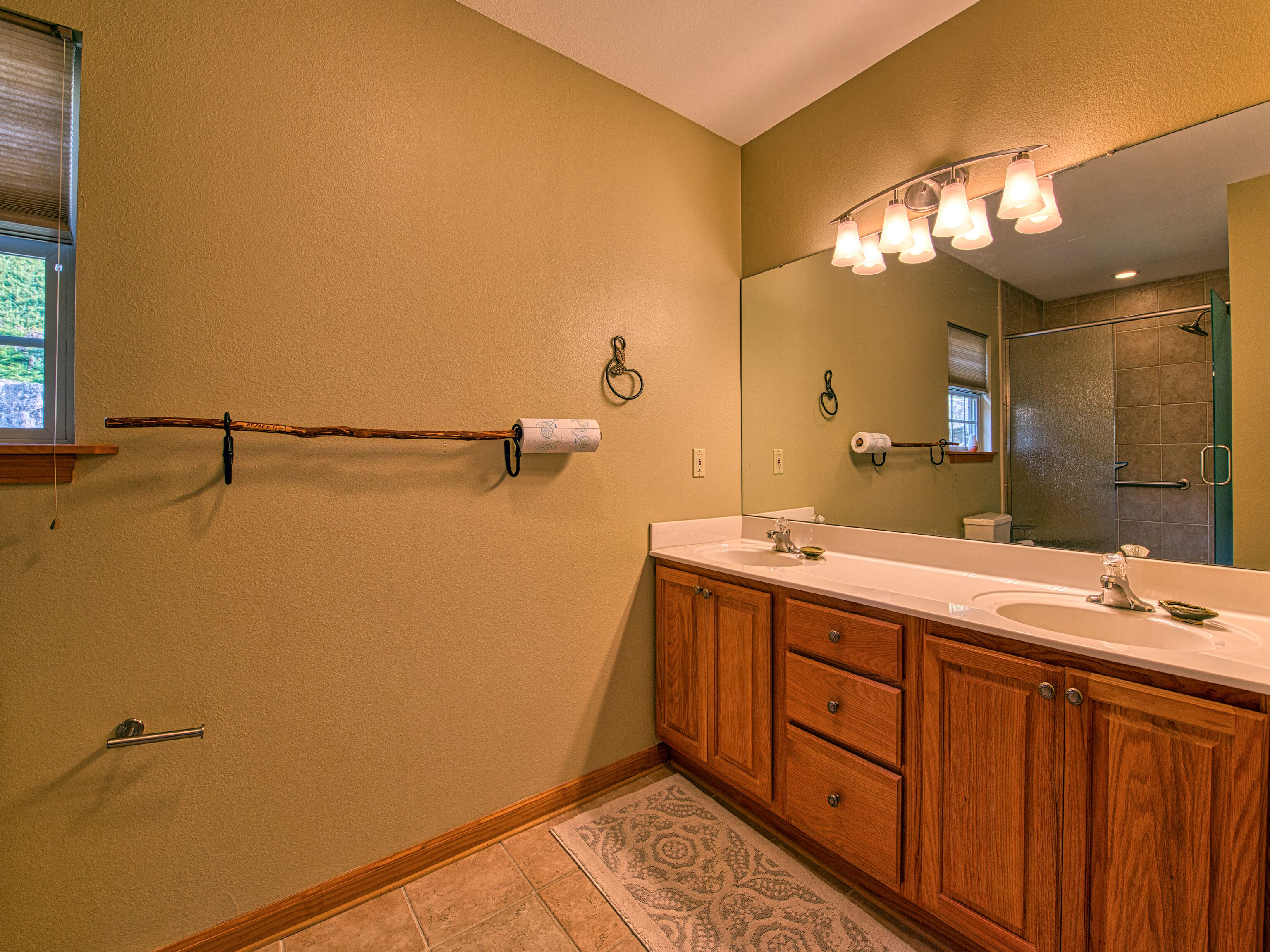 A bathroom with a wooden vanity, two sinks, a large mirror, and a shower.