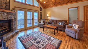 A spacious living room with a stone fireplace, wooden ceiling, and large windows. - 2 BD 2 BA Cottage, Paved Access, Close to Town, Super Views, Cable, WIFI, (Waynesville)