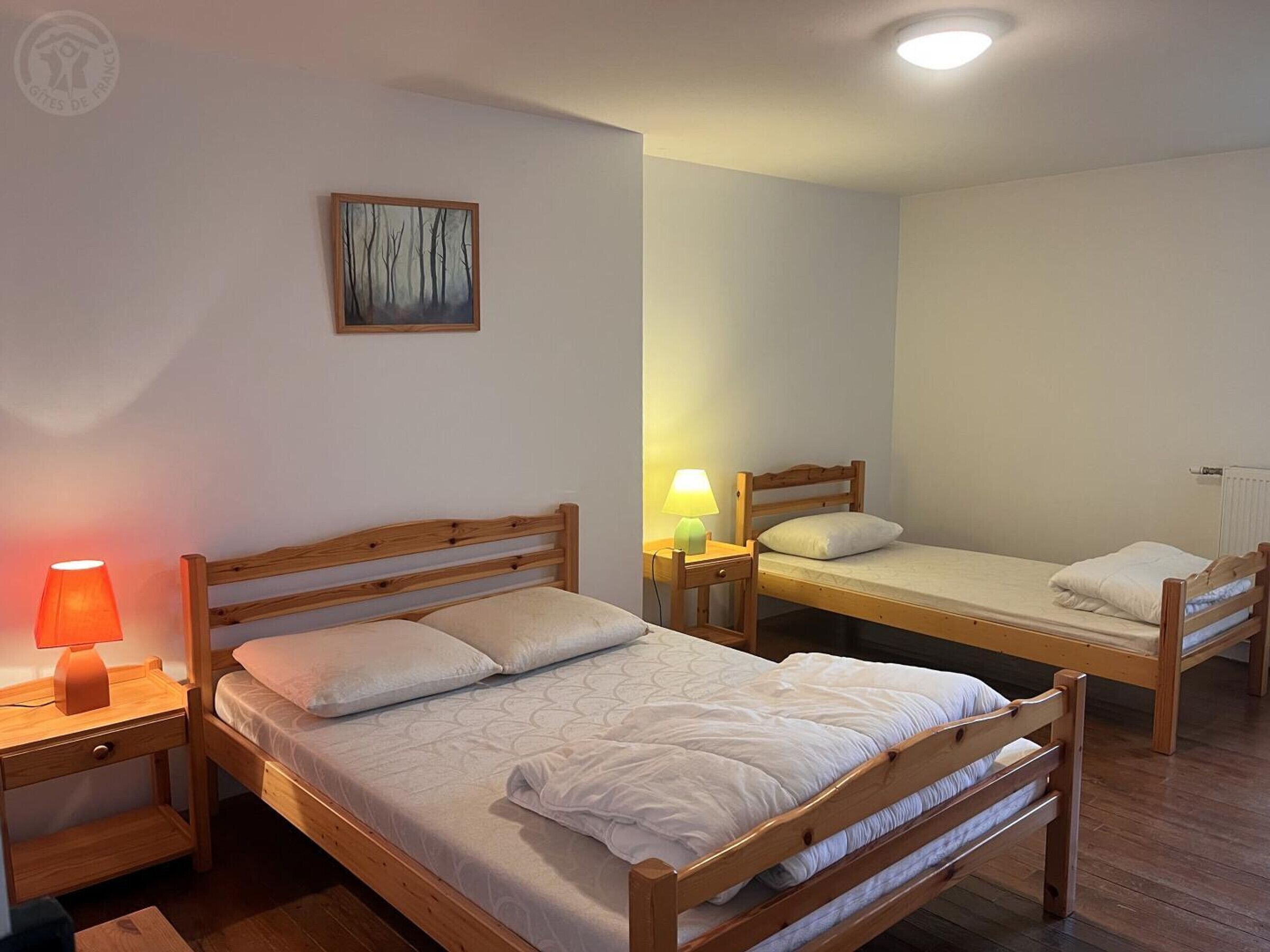 Une chambre avec deux lits superposés en bois, une table de chevet avec une lampe, un tableau au mur et un radiateur.
