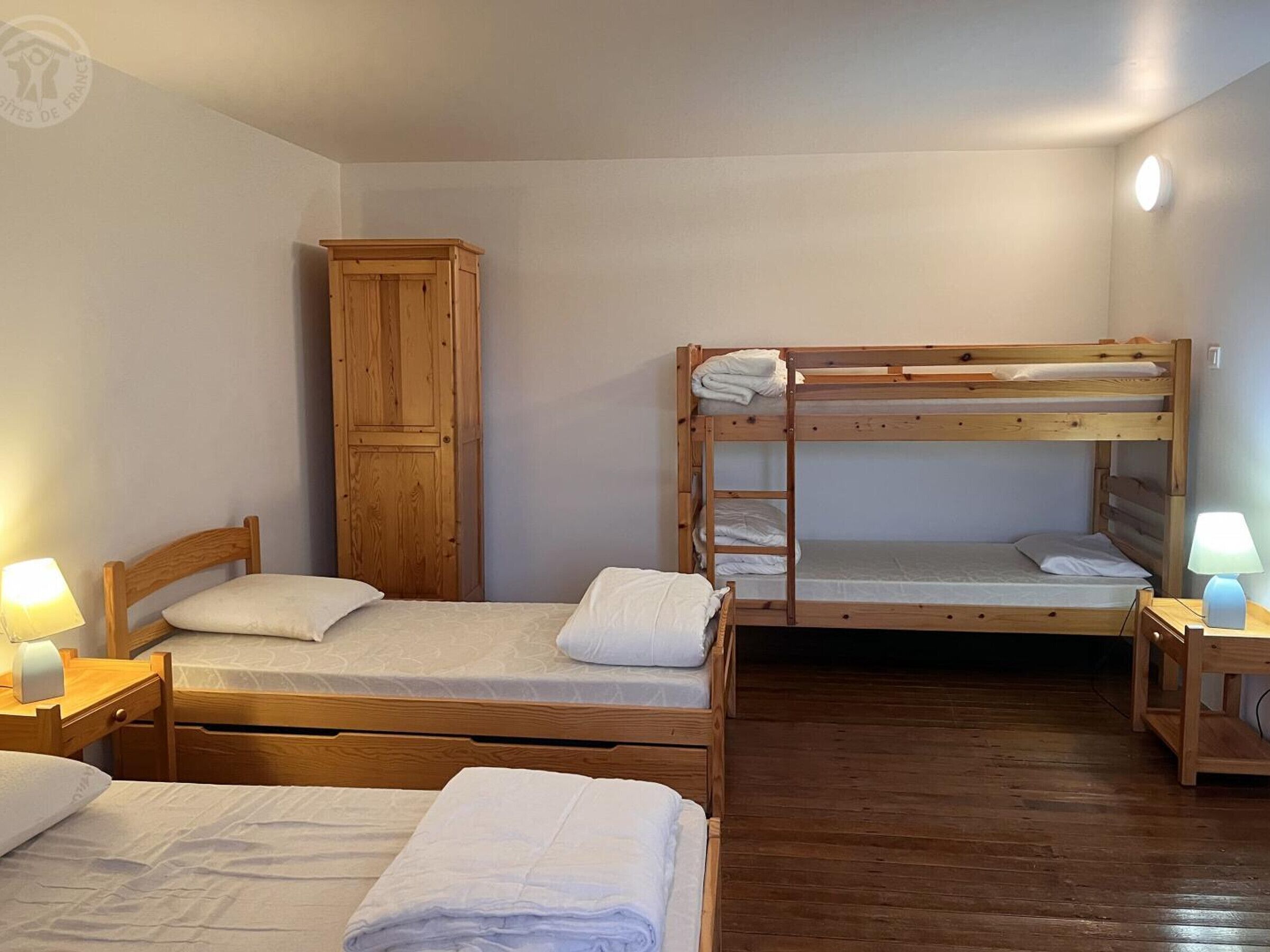 A dormitory room with bunk beds, a wooden wardrobe, and bedside lamps.