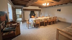 Een landelijke eetkamer met een grote houten tafel, stoelen en een stenen open haard.