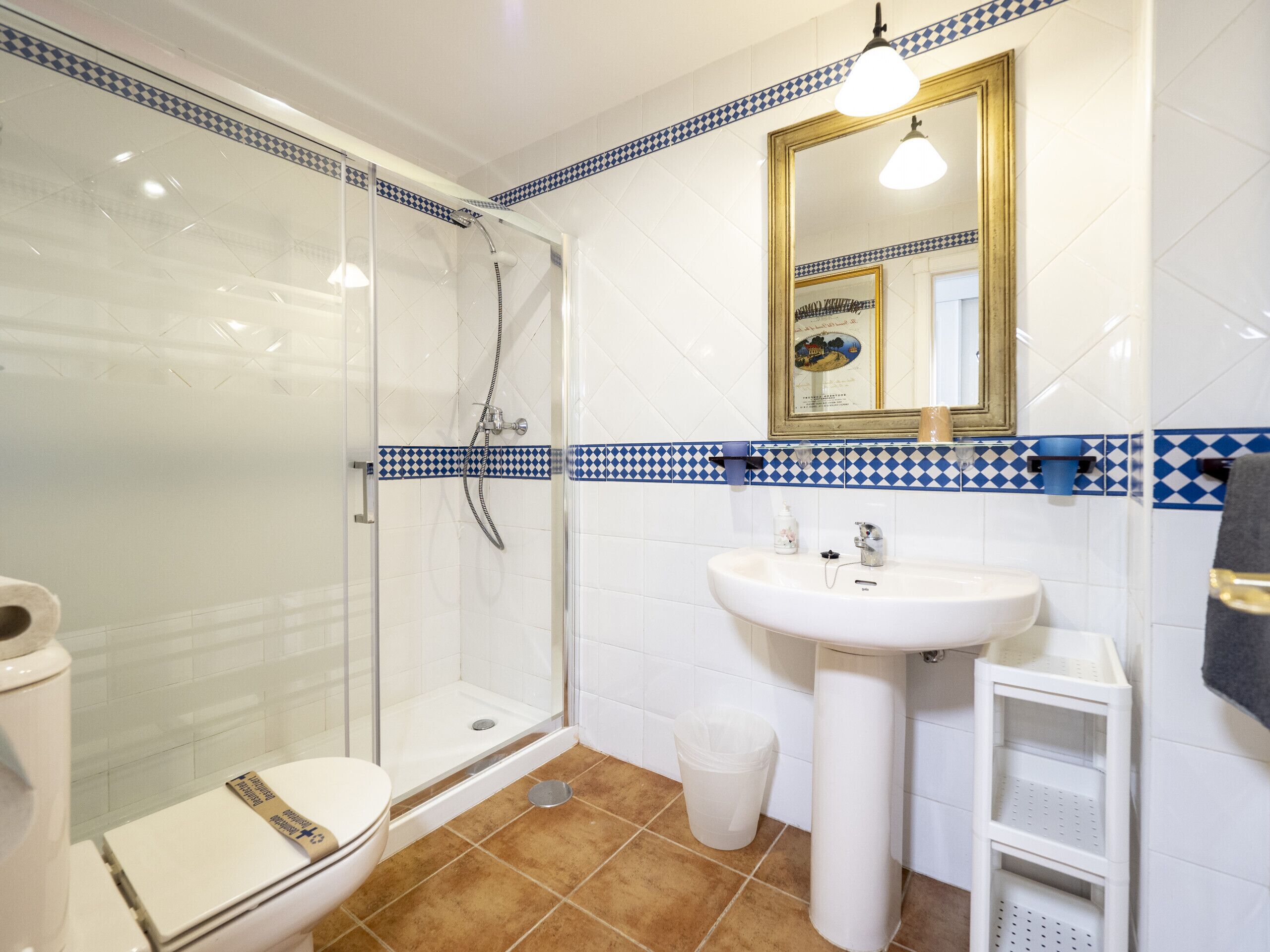 A bathroom with a glass shower enclosure, a white sink, and a tiled floor.