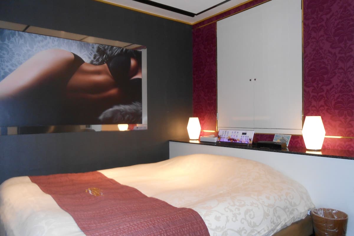 Quarto de hotel com cama, um espelho grande, duas luminárias de cabeceira e uma TV fixada na parede.