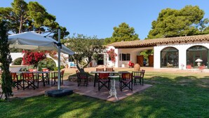 Une terrasse extérieure avec des tables et des chaises, un parasol blanc et un bâtiment doté d’un toit en tuiles.