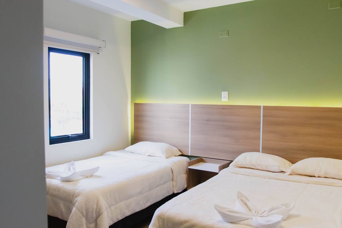A hotel room with two single beds, a wooden headboard, a window, and a bedside table.