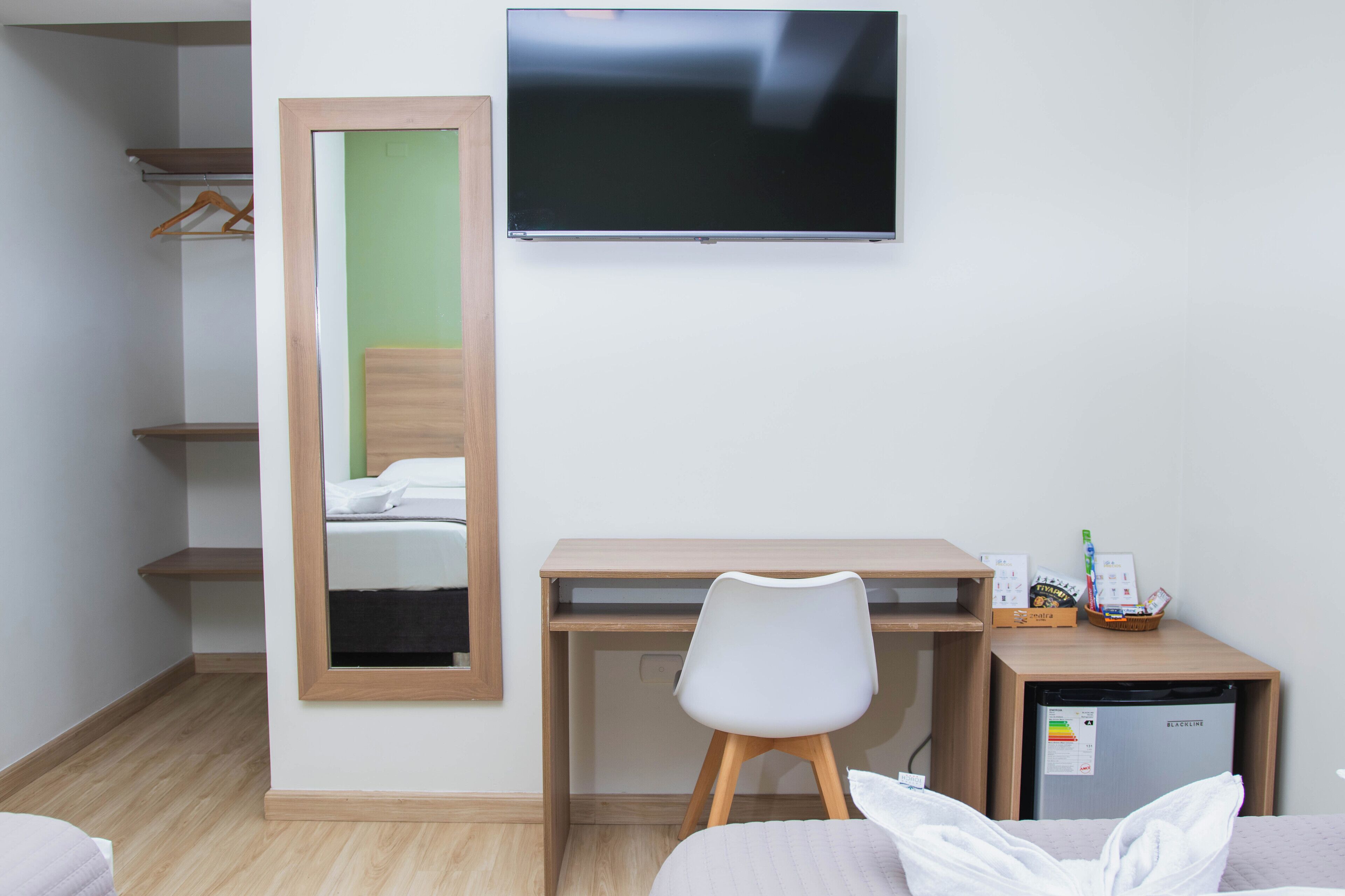 Een hotelkamer met een bed, een bureau met stoel, een televisie, een kleine koelkast en een spiegel.