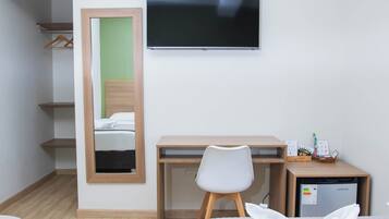 Een hotelkamer met een bed, een bureau met stoel, een televisie, een kleine koelkast en een spiegel.