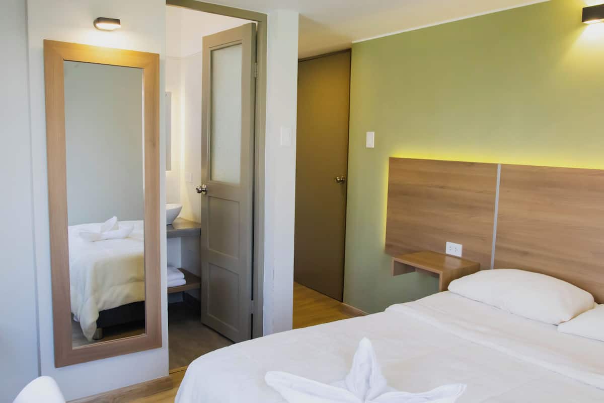 A hotel room with a bed, a bedside table, a mirror, and a door leading to a bathroom.