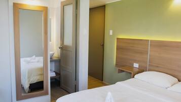 A hotel room with a bed, a bedside table, a mirror, and a door leading to a bathroom.