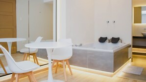 Un baño moderno con una bañera grande, ducha y un lavamanos blanco. En primer plano, hay una pequeña mesa con sillas.