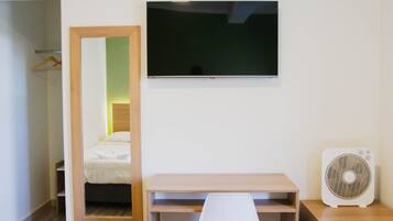 Habitación de hotel con cama, escritorio, silla, televisor y ventilador.
