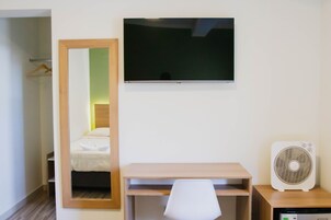 Habitación de hotel con cama, escritorio, silla, televisor y ventilador.