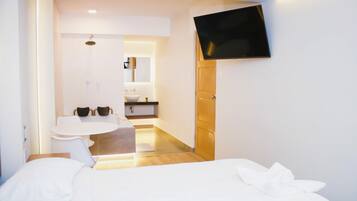 A hotel room with a bed, a TV mounted on the wall, a bathroom with a sink and mirror, and a small table with chairs.