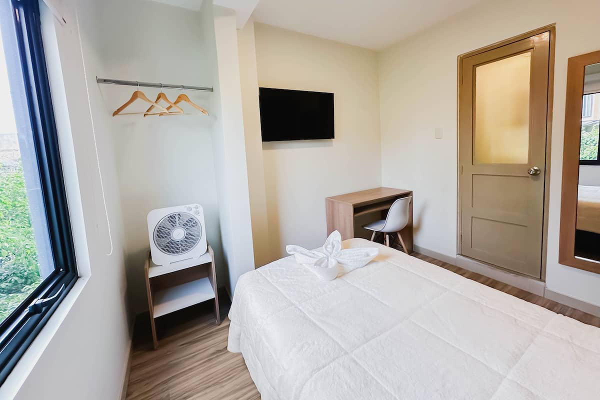 A bedroom with a bed, a desk, a chair, a TV, and a wardrobe.
