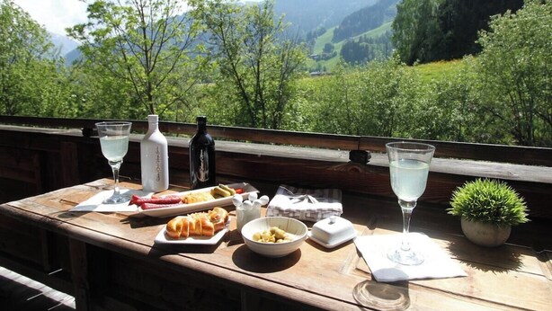 A wooden table with food, drinks, and a small potted plant, overlooking a mountainous landscape. - Chalet Belle Kitz 1 by belle-stay (Kitzbühel)