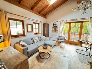 Una sala de estar acogedora con un sofá seccional gris, una mesa de centro de madera y una zona de comedor con mesa y sillas.