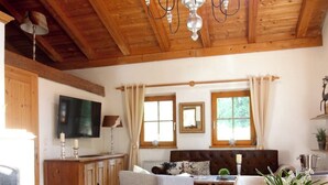 A wooden interior with a dining table, chairs, a sofa, a TV, and a chandelier. - Chalet Belle Kitz 1 by belle-stay (Kitzbühel)